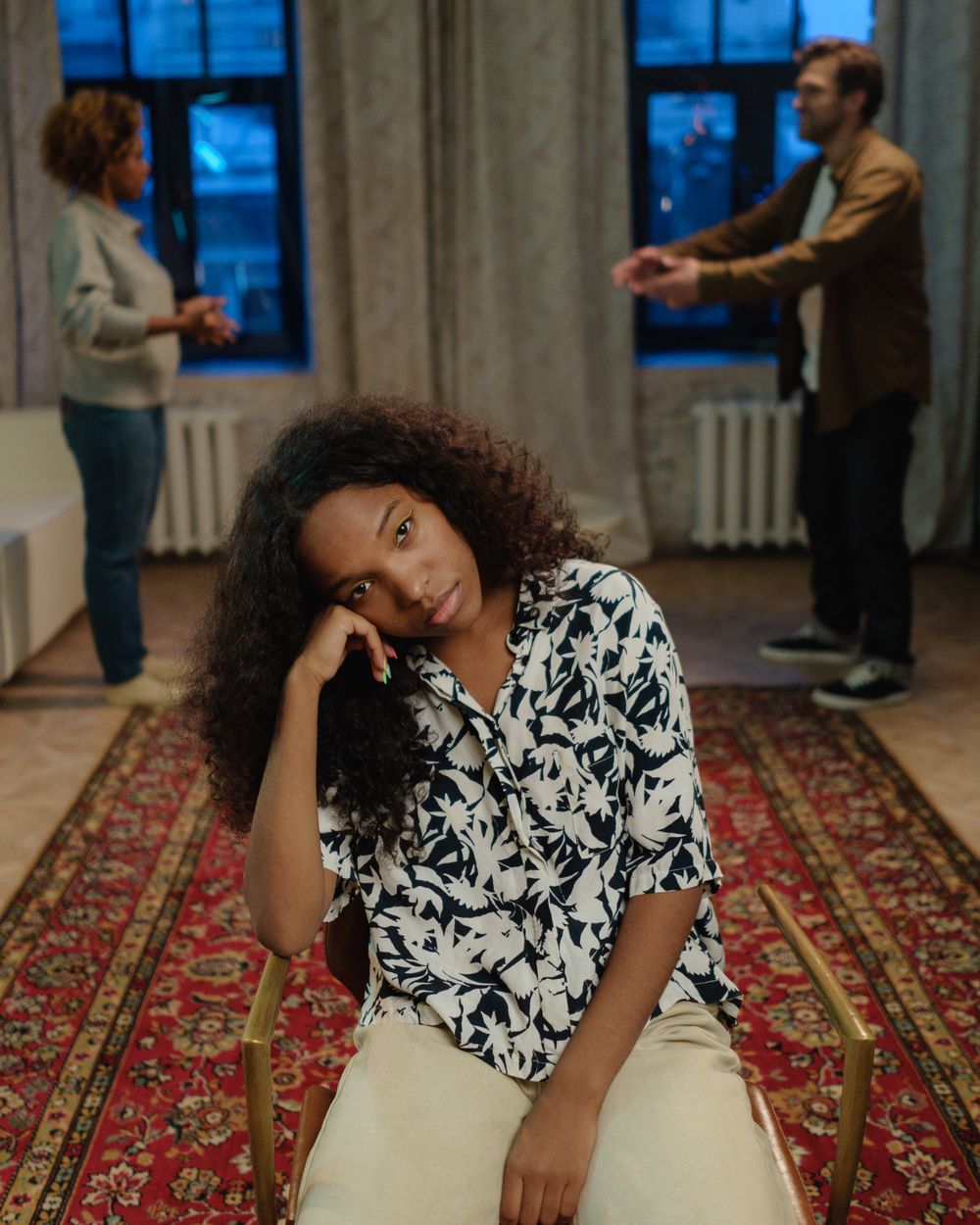 A teenager sitting apart while two adults argue behind her