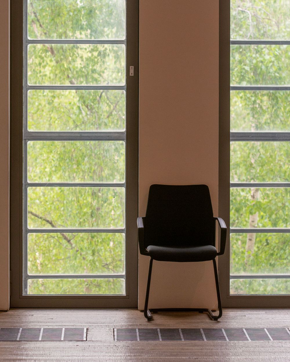 A single chair beside tall windows looking out onto trees
